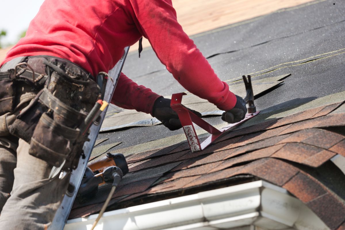 A man performing roofing work, using a tool to install or repair a roof, showcasing professional roofing services.