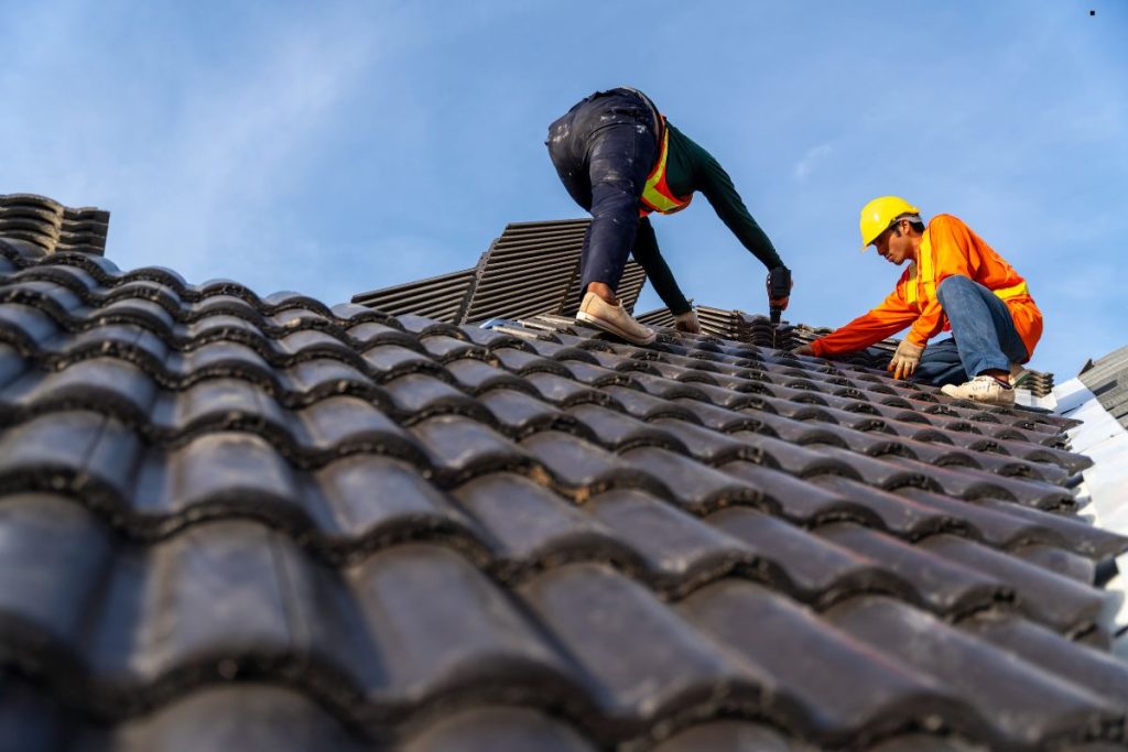 Two men performing roofing work on a tiled roof, showcasing professional roofing services in action.