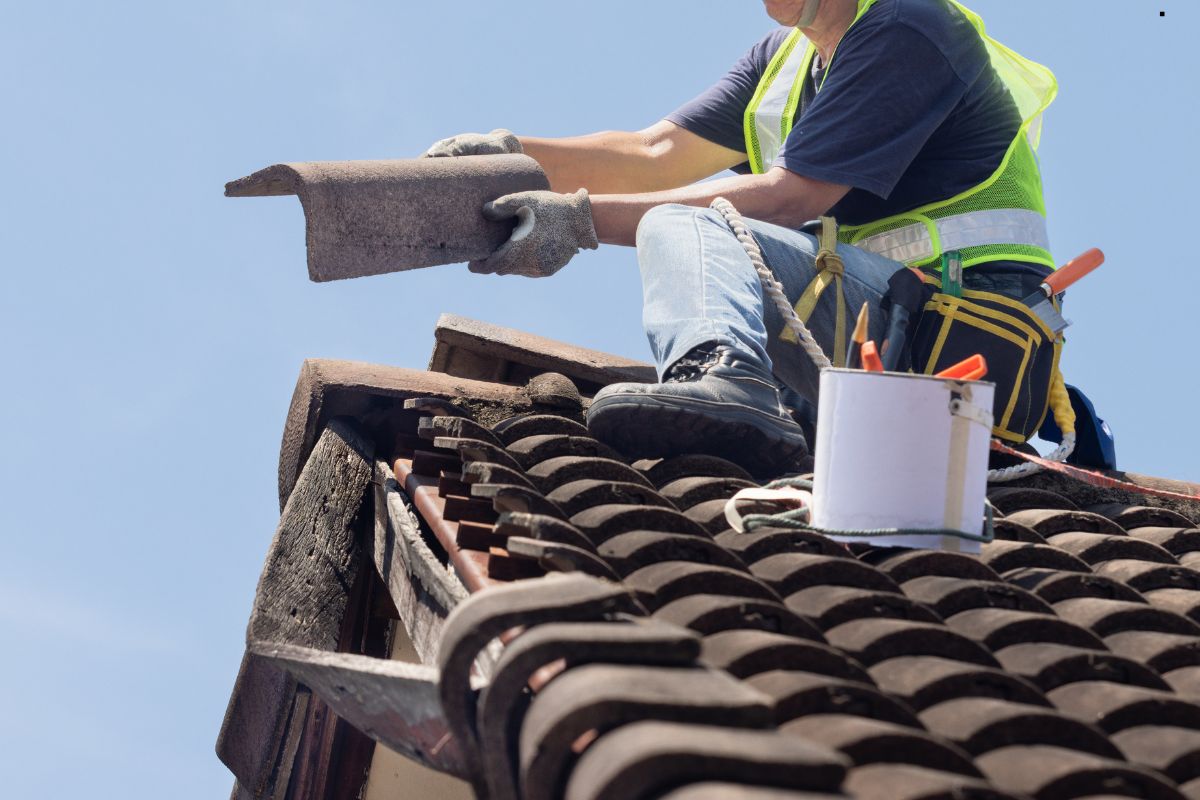  A man performing roofing services on a roof, equipped with a tool and a bucket for repairs.