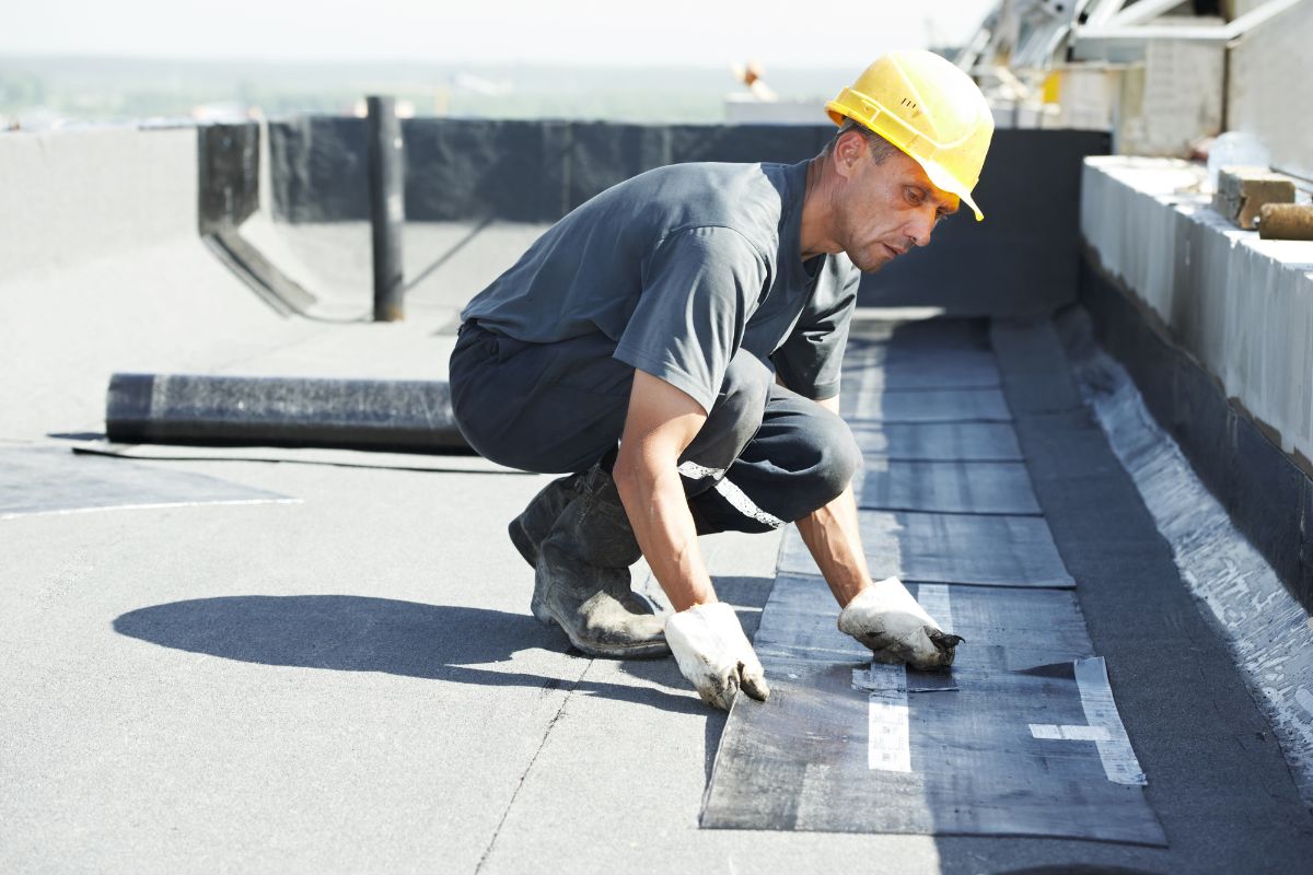 A man wearing a hard hat and safety vest is working on a roof, ensuring safe access for heavy equipment.