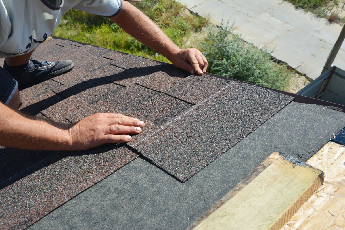 A man installs a roof shingle on a house, demonstrating safe heavy equipment roof access practices.